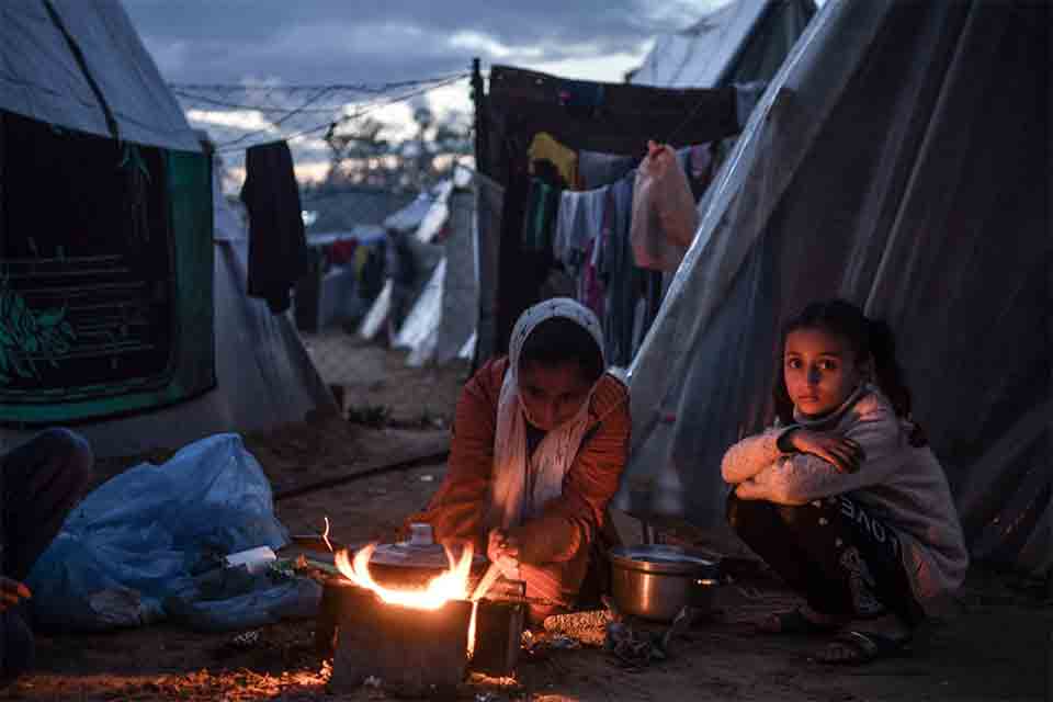 해질 무렵 천막 사이에 두 사람이 앉아 있다. 앞에는 솥을 걸어둔 모닥불이 있다. 한 사람을 불을, 한 사람은 카메라를 보고 있다. 뒤로는 다른 천막들과 빨래가 널린 빨랫줄이 보인다.