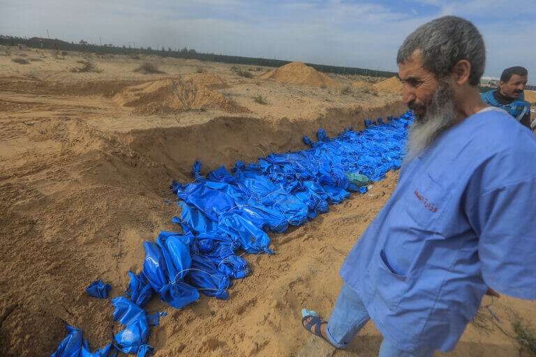 모래밭에 길게 판 고랑에 푸른 천으로 싼 무언가가 줄 지어 놓여 있다. 위쪽에 선 한 사람이 이를 내려다보고 있다.